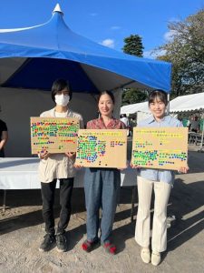 3人が段ボールを持って立っている。段ボールにはアンケートの問いと回答の選択肢が書いてあり、シールが貼ってある